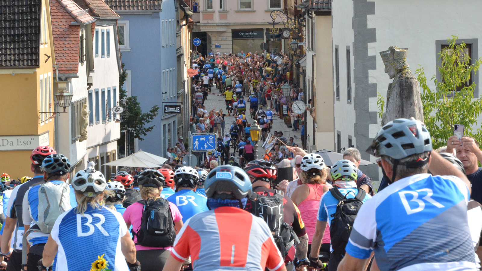 Impression der BR-Radltour 2025 Eine große Gruppe Radlerinnen und Radler fährt durch eine enge Gasse